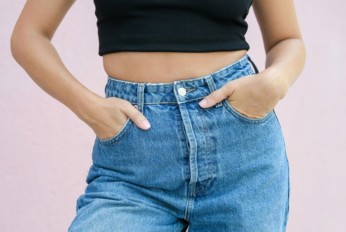 Woman wearing trendy high-waisted jeans with hands in pockets, showcasing disliked fashion trends.