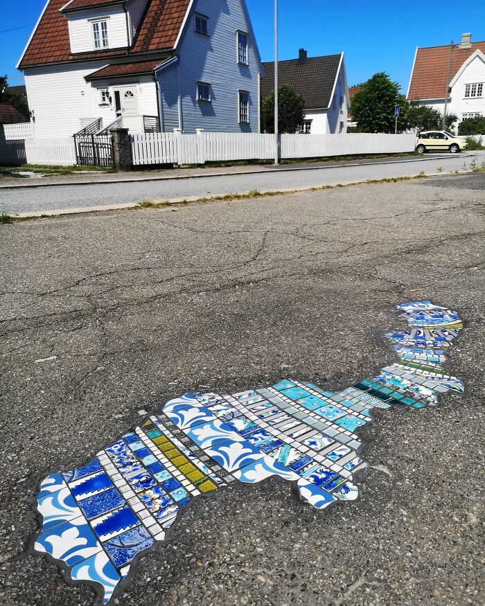 Vibrant mosaic art fills a c*****d sidewalk, showcasing an artist's creative repair on a residential street.