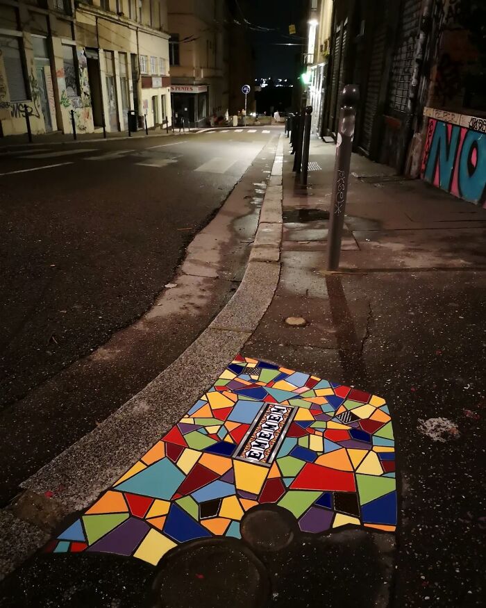 C*****d sidewalk repaired with vibrant mosaic art at night.
