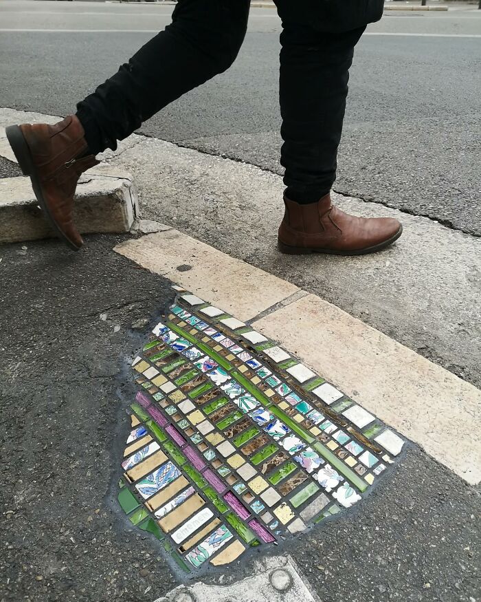 Vibrant mosaic art repairs c*****d sidewalk while a person in brown boots walks by.