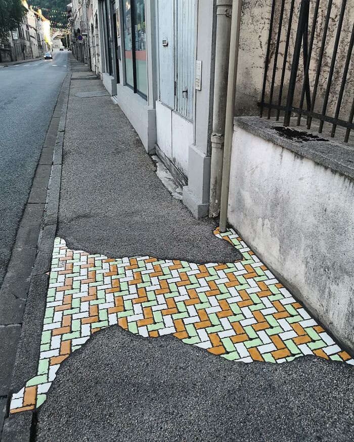 Vibrant mosaic repairs a c*****d sidewalk, blending art with urban landscape on a quiet street.