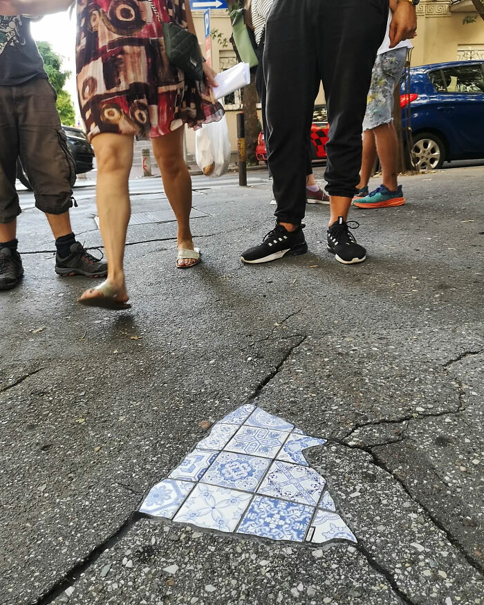 Vibrant mosaic art fills a c*****d sidewalk, surrounded by pedestrians.