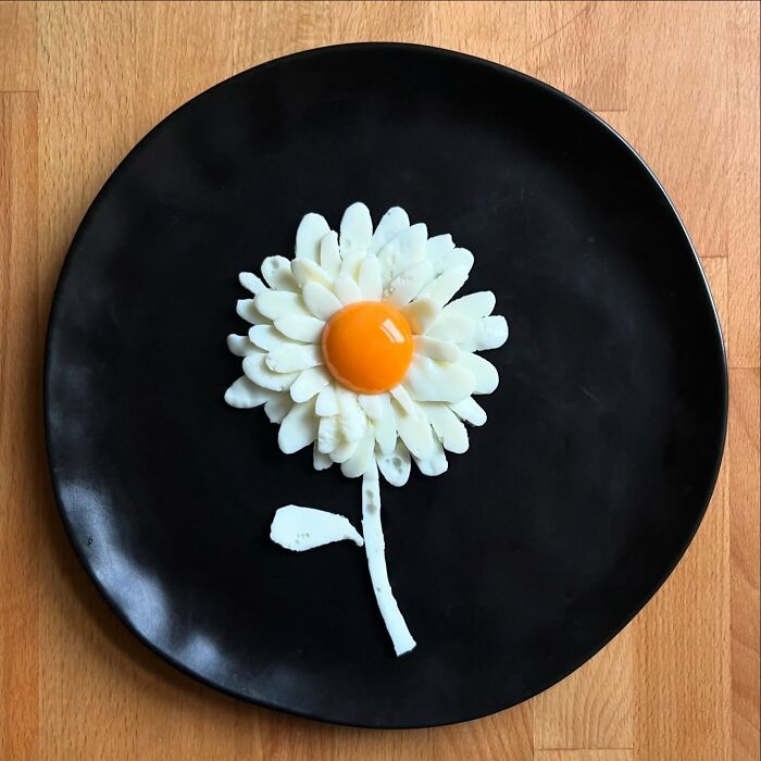 Creative egg design resembling a flower on a black plate, showcasing unique ways the artist has fried eggs.