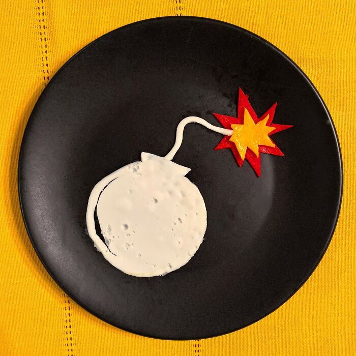 Creative egg art shaped like a b**b with a lit fuse on a black plate.