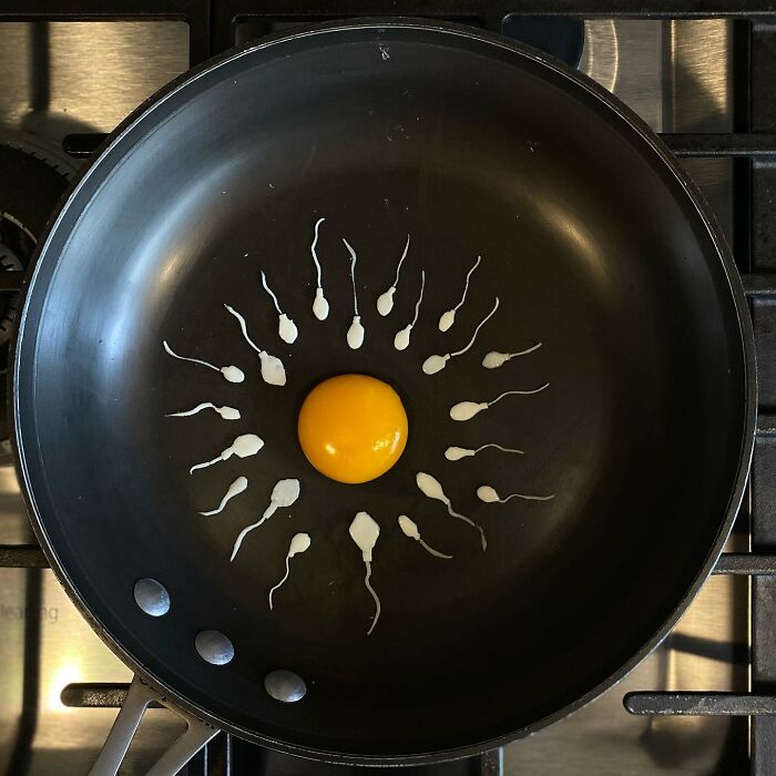 Creative egg art in frying pan with yolk surrounded by s***m shapes.