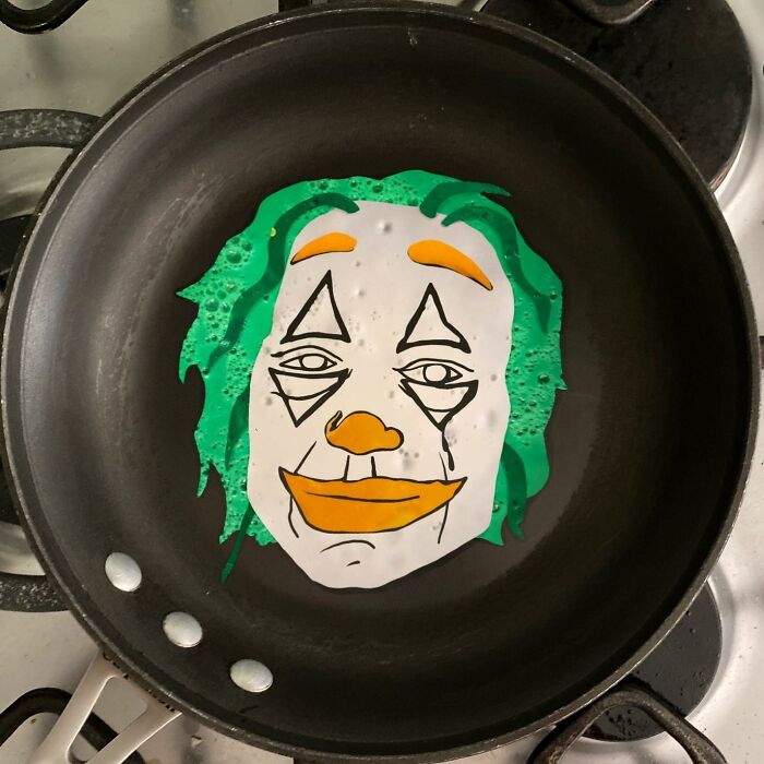 Creative egg art depicting a clown face being fried in a pan.