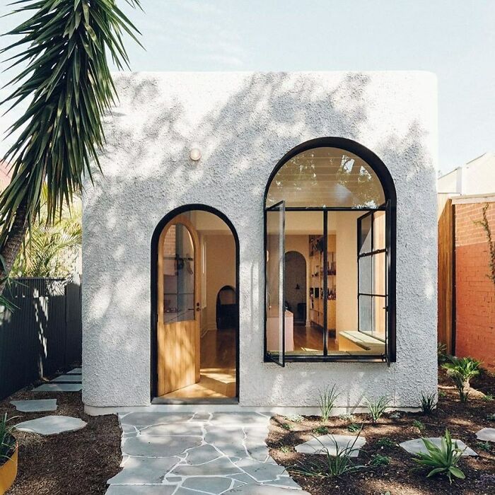 Modern tiny home exterior with arched windows, surrounded by garden plants, showcasing minimalist design.