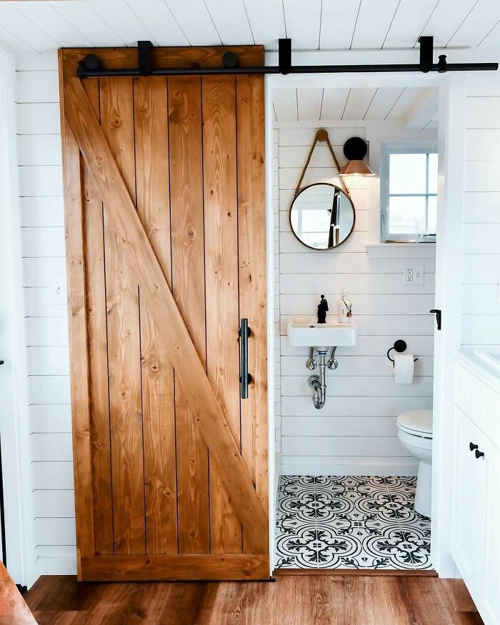 Cozy tiny home bathroom with rustic wood door, round mirror, and patterned tile floor.