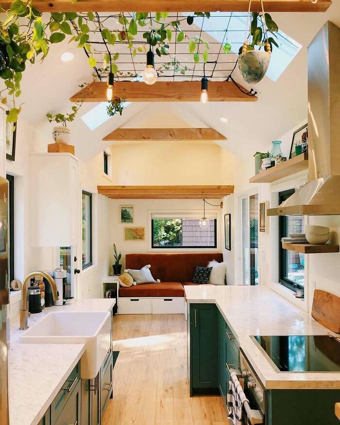 Interior view of a cozy tiny home kitchen with green cabinets and hanging plants.