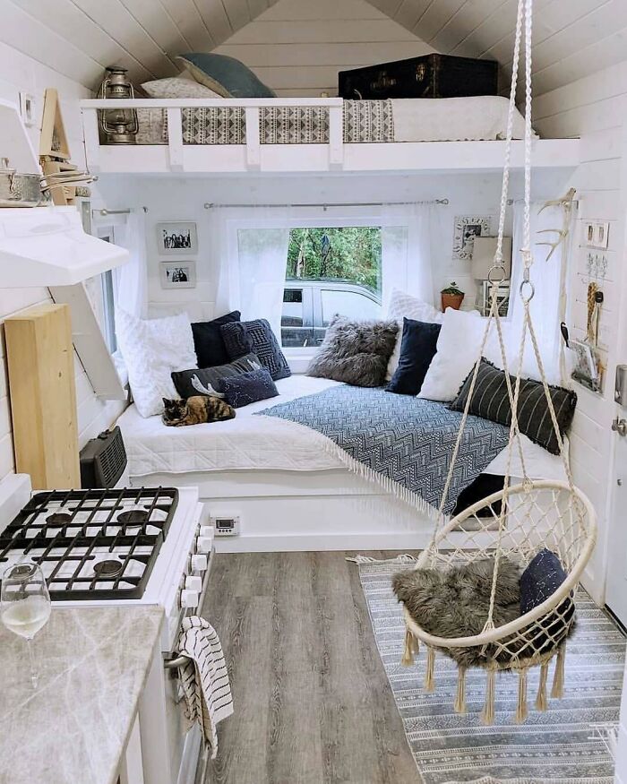 Cozy interior of a dreamy tiny home with a loft bed, hammock chair, and soft pillows.