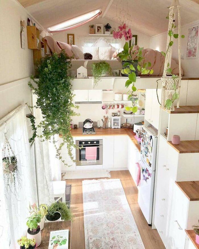 Cozy interior of a dreamy tiny home featuring plants, a compact kitchen, and a lofted bed.