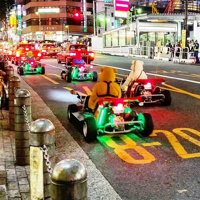 People dressed as video game characters drive go-karts on a city street at night.