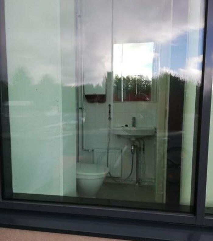 Bathroom with a toilet and sink visible through a large window, showcasing a construction error.
