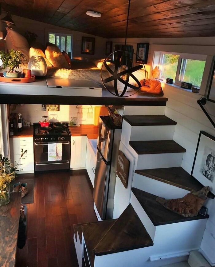 Cozy wooden interior of a tiny home with compact kitchen and loft bed, flooded with warm natural light.