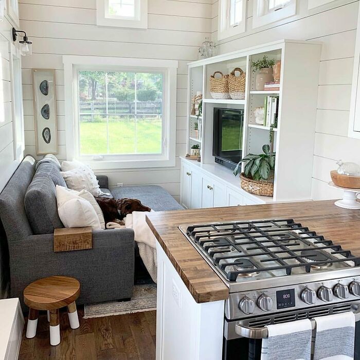 Cozy interior of a tiny home with a sofa, stove, and built-in shelving in a bright, airy space.