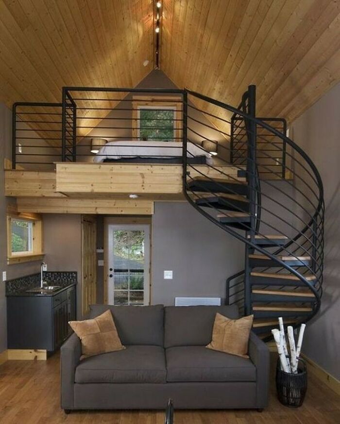 Tiny home interior with a loft bed, spiral staircase, and modern decor.