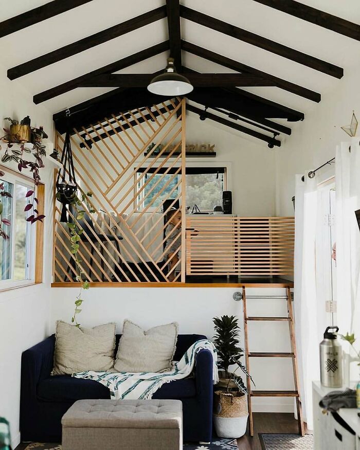 Tiny home interior with a loft area, wooden accents, cozy sofa, and potted plants, showcasing efficient small space design.