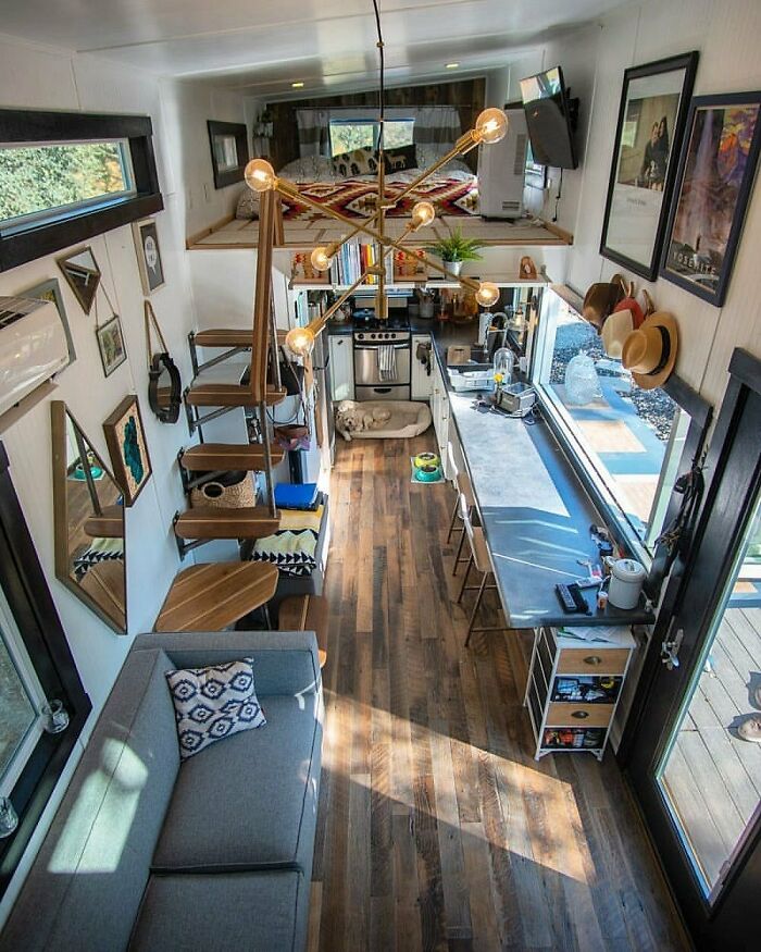 Dreamy tiny home interior with modern decor, loft bed, small kitchen, and cozy living area featuring a stylish chandelier.