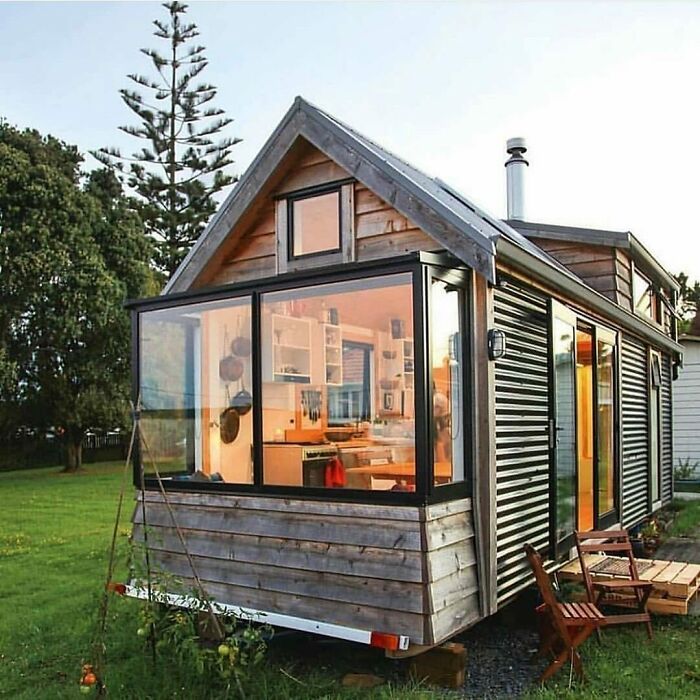 Cozy tiny home with large windows, surrounded by greenery and a small patio.