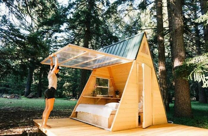 A-frame tiny home with a retractable roof in a forest setting, showcasing minimalist design and cozy living space.