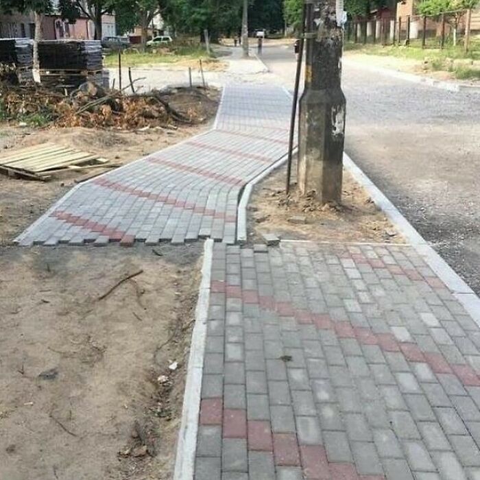 Construction workers misalign sidewalk around a pole, showcasing a comical mishap in construction.