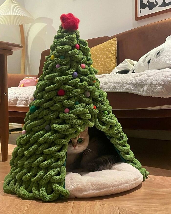 Cat cozy under a knitted Christmas tree, showcasing a unique holiday decor idea.