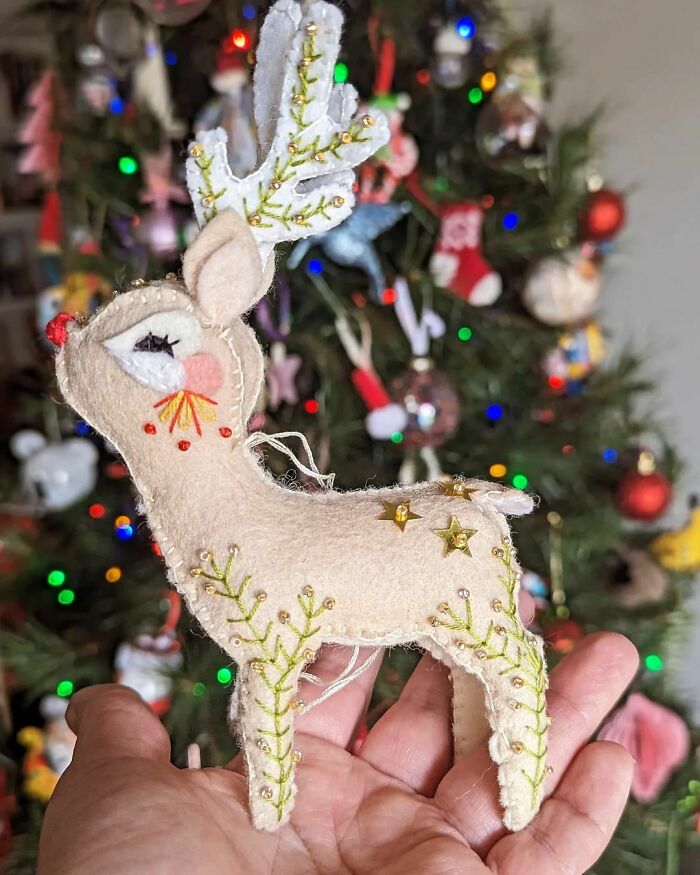 Handmade felt reindeer ornament for DIY Christmas decorations, held in front of a decorated Christmas tree.
