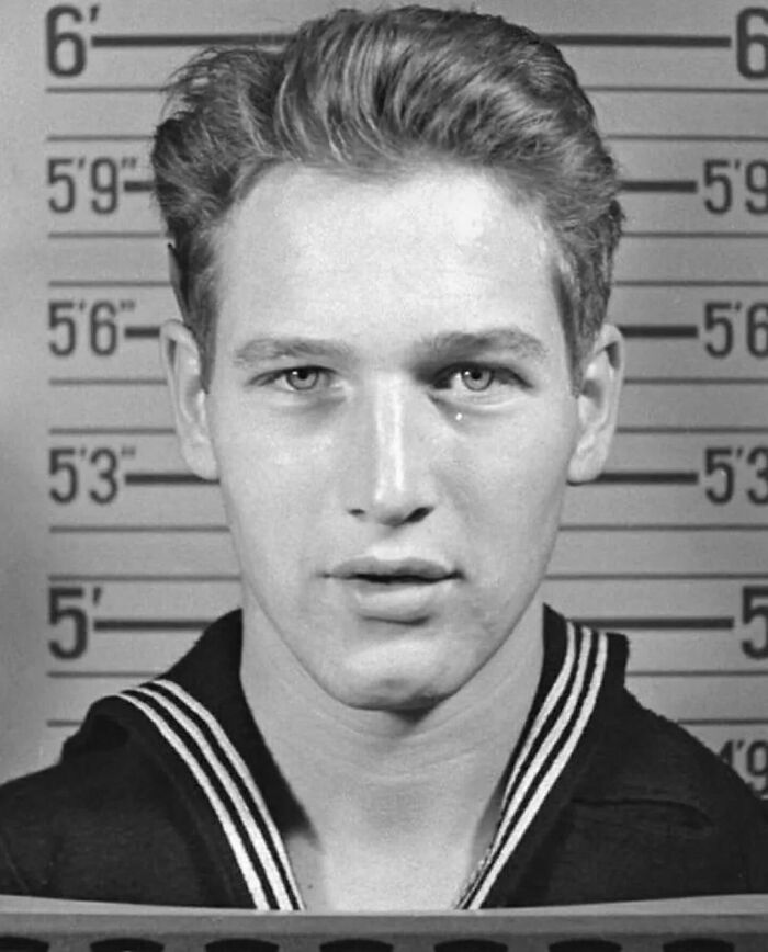 Young man in naval uniform in front of height chart, historical photograph.