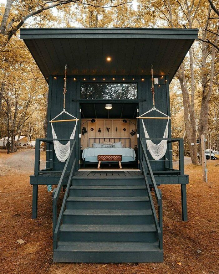 Tiny home with cozy porch in a wooded setting, featuring hammocks and a bed inside.