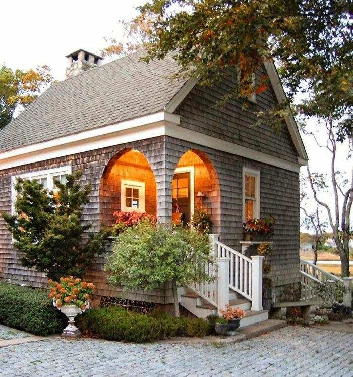 Charming tiny home with rustic exterior, warm lighting, and inviting front porch surrounded by greenery.