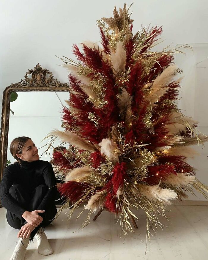 Woman sitting beside a creative Christmas tree decorated with red and golden pampas grass.