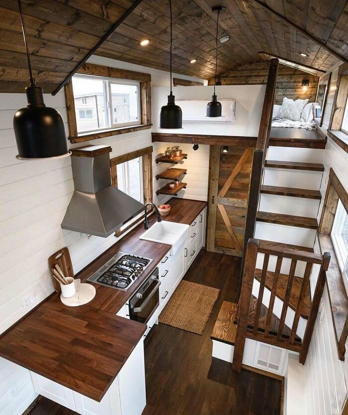 Tiny home interior with modern kitchen, wooden accents, and lofted bed area.