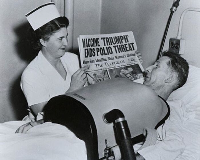 Nurse shows patient historic newspaper about polio vaccine triumph, demonstrating learning from the past.