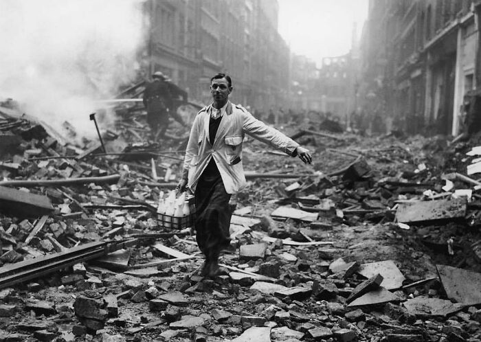 Man walking through rubble carrying milk bottles, a historical scene depicting resilience amidst destruction.