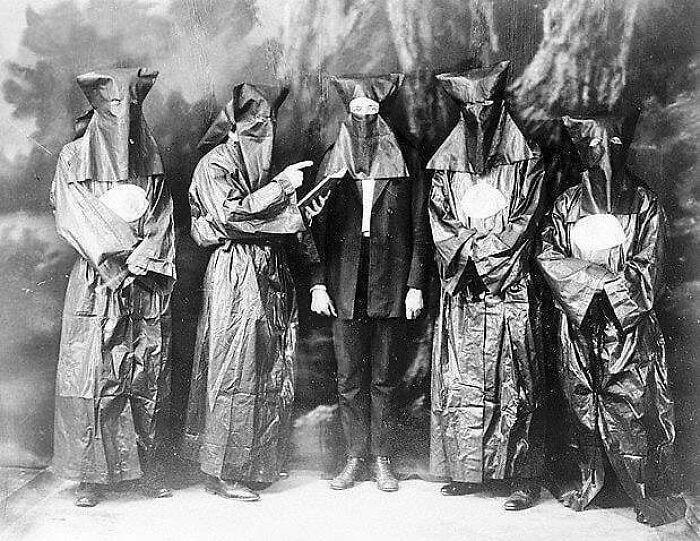Five masked individuals in robes posing in a historical black and white photo, highlighting learn from the past themes.