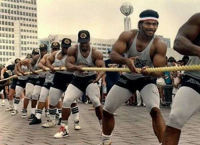 Bodybuilders in a tug-of-war competition, showcasing historical strength and teamwork in an urban setting.