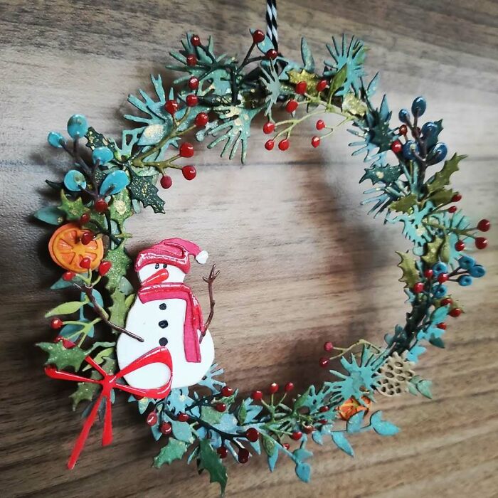 DIY Christmas wreath with a snowman, pine leaves, and berries on a wooden background.