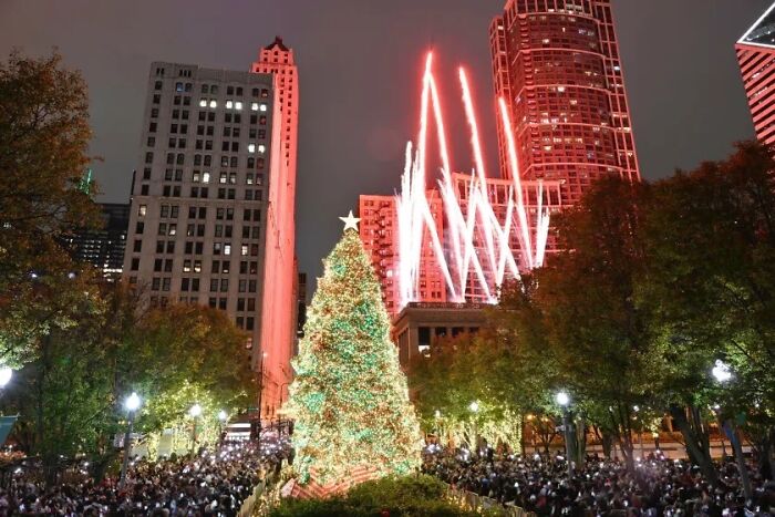 Christmas tree in a city square with fireworks illuminating the night sky.
