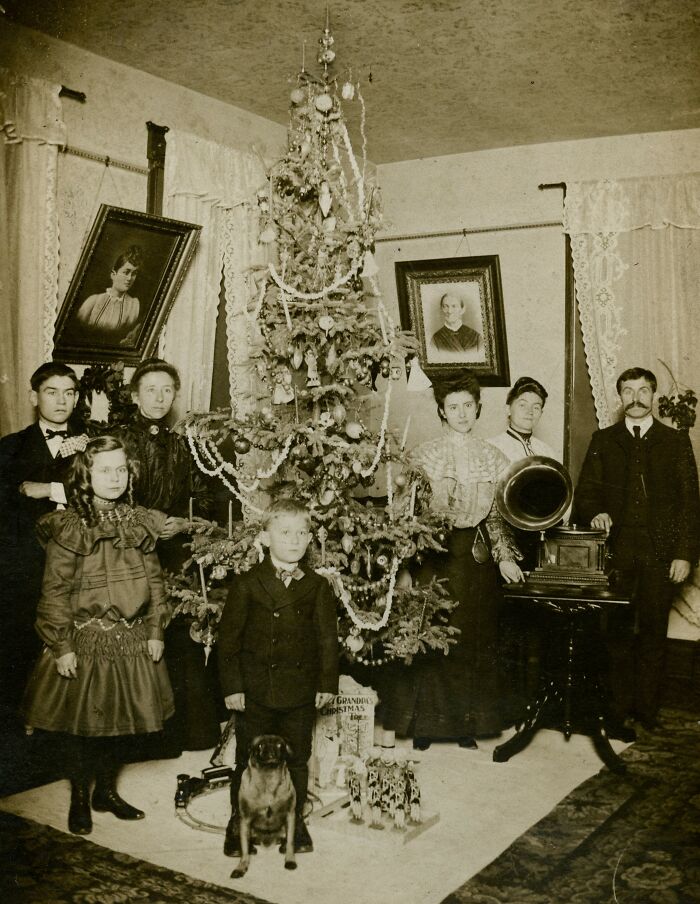 Victorian family posing with a decorated Christmas tree in a historical setting, featuring period decor and a gramophone.