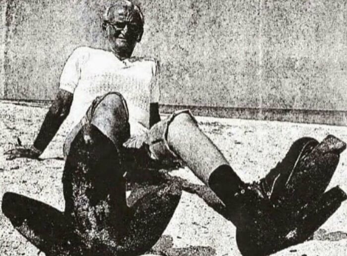 Man wearing large diving flippers, sitting on sand, a glimpse into interesting history facts.