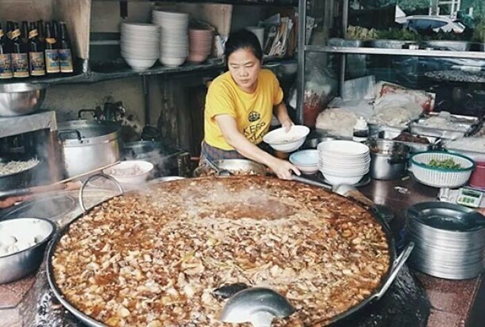 Woman cooking large traditional dish in a street food stall, showcasing interesting history and culinary facts.