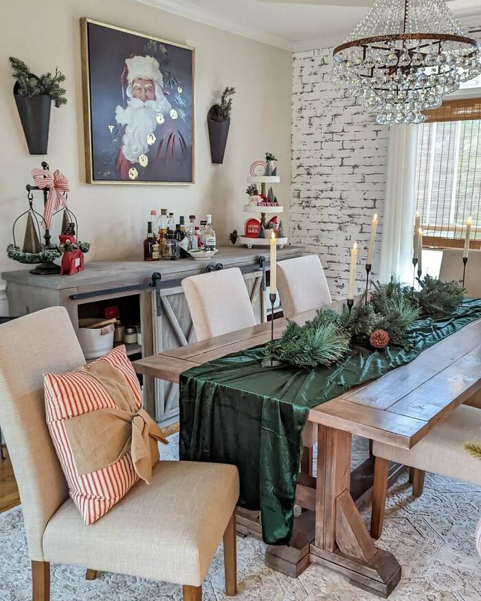 Dining room with Christmas-decorating-ideas: Santa painting, rustic table with greenery, candles, and festive touches.
