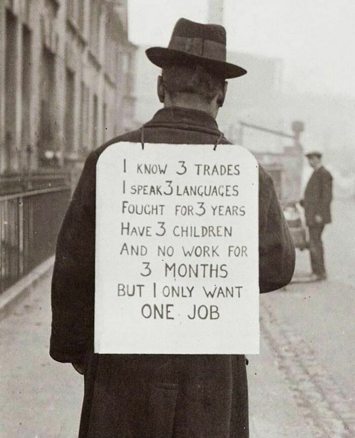 Man in vintage attire with a sign expressing unemployment struggle, a poignant historical image reflecting past economic hardships.