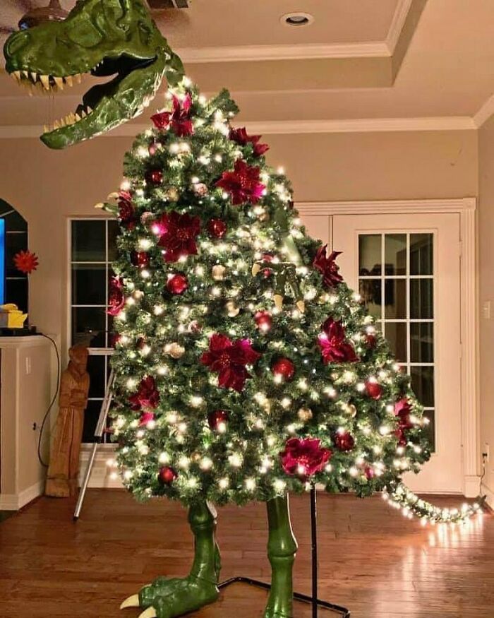 Dinosaur themed Christmas tree decorated with lights and ornaments, featuring a T-Rex head and legs for a humorous prehistoric touch.