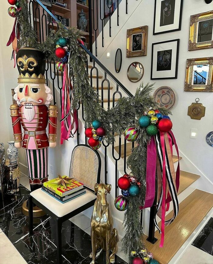Nutcracker and garland with baubles and ribbons adorn a staircase in a festive Christmas-decorating display.