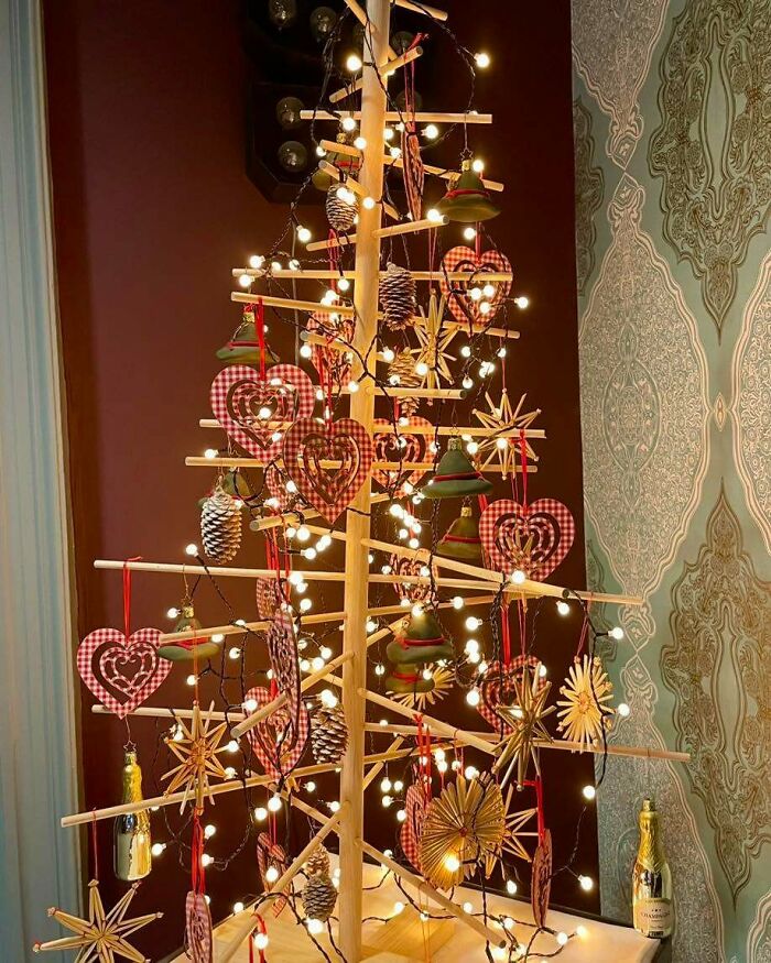 DIY Christmas tree with wooden branches, adorned with lights, red hearts, stars, and pinecones.