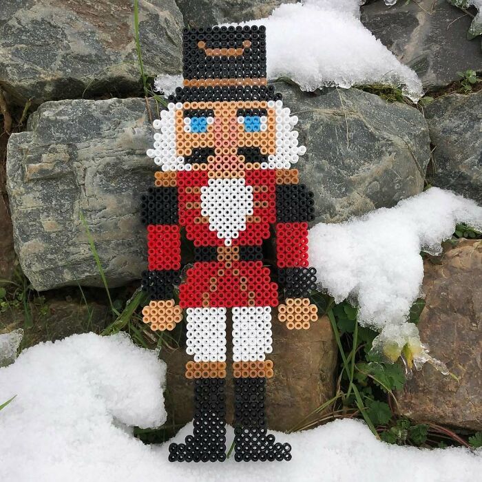 Nutcracker made from beads, part of creative DIY Christmas decorations, against a snowy stone background.