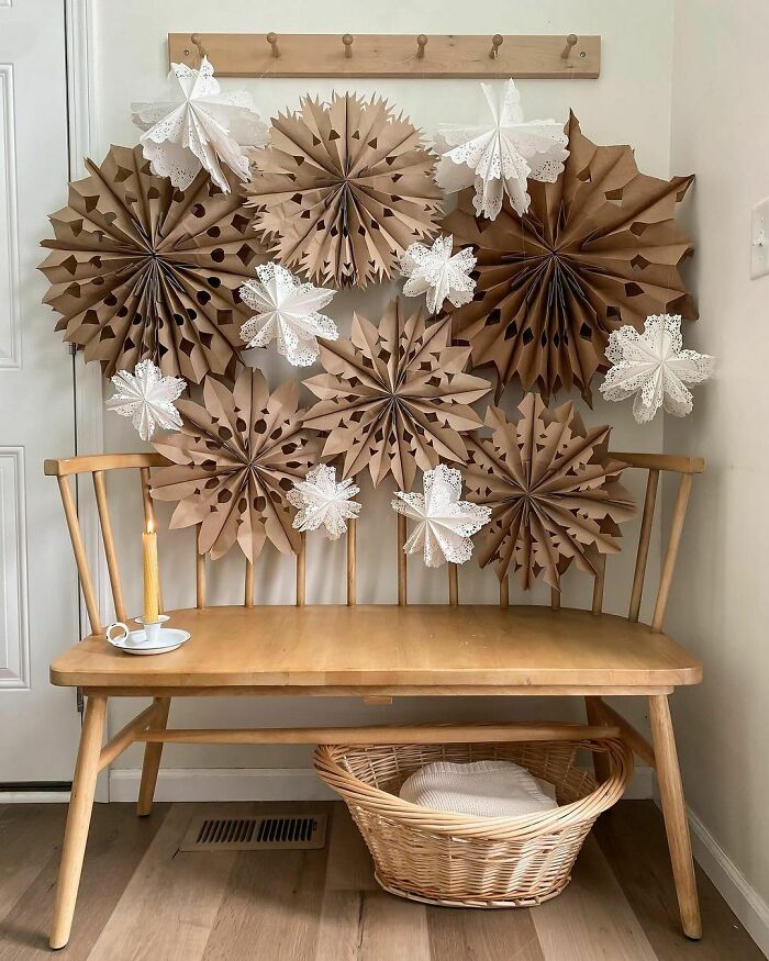 DIY Christmas decorations made of paper snowflakes above a wooden bench with a candle and teacup.