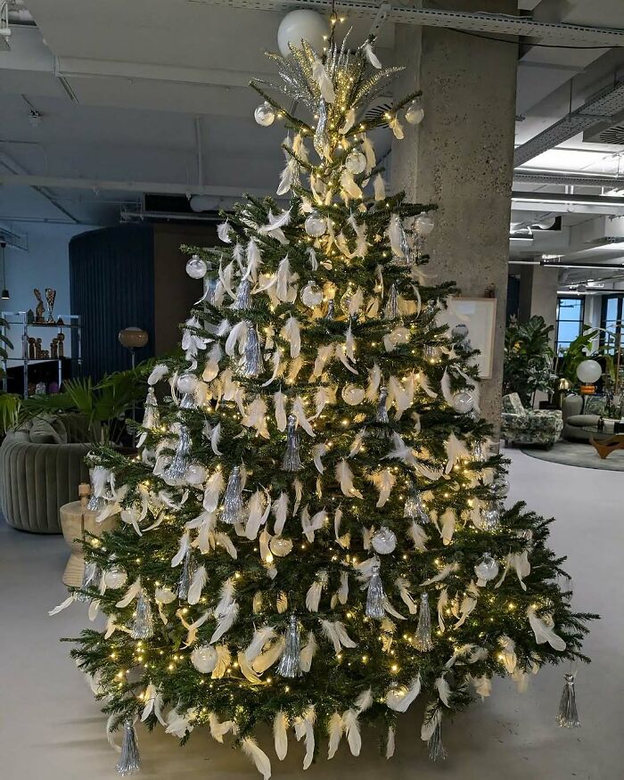 Festive Christmas tree decorated with white feathers and silver ornaments in a modern living room setting.