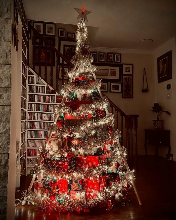 Creative Christmas tree decorated with tinsel and gifts, arranged on a wooden ladder, glowing warmly in a cozy room.
